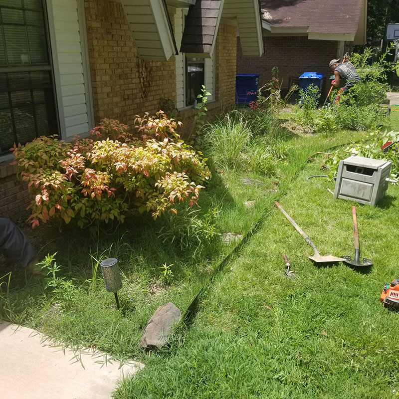 landscape professional working on landscaping in front of brick home